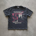 May include: A black t-shirt with a white graphic print of Jake Gyllenhaal from the movie Donnie Darko. The graphic includes the movie title 'Donnie Darko' in pink and white text, a quote from the movie, and a black and white image of Jake Gyllenhaal.